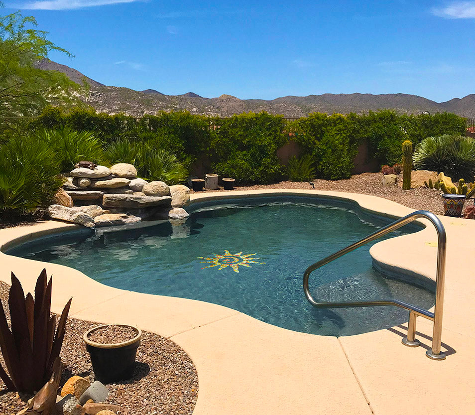 Pool area with a sun-shaped mosaic, surrounded by greenery and mountains.