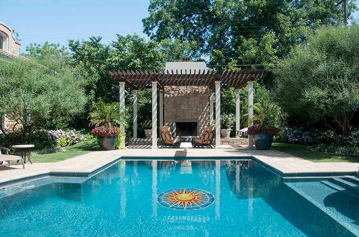 Pool with decorative mosaic, lounge chairs, and a gazebo in a garden setting.